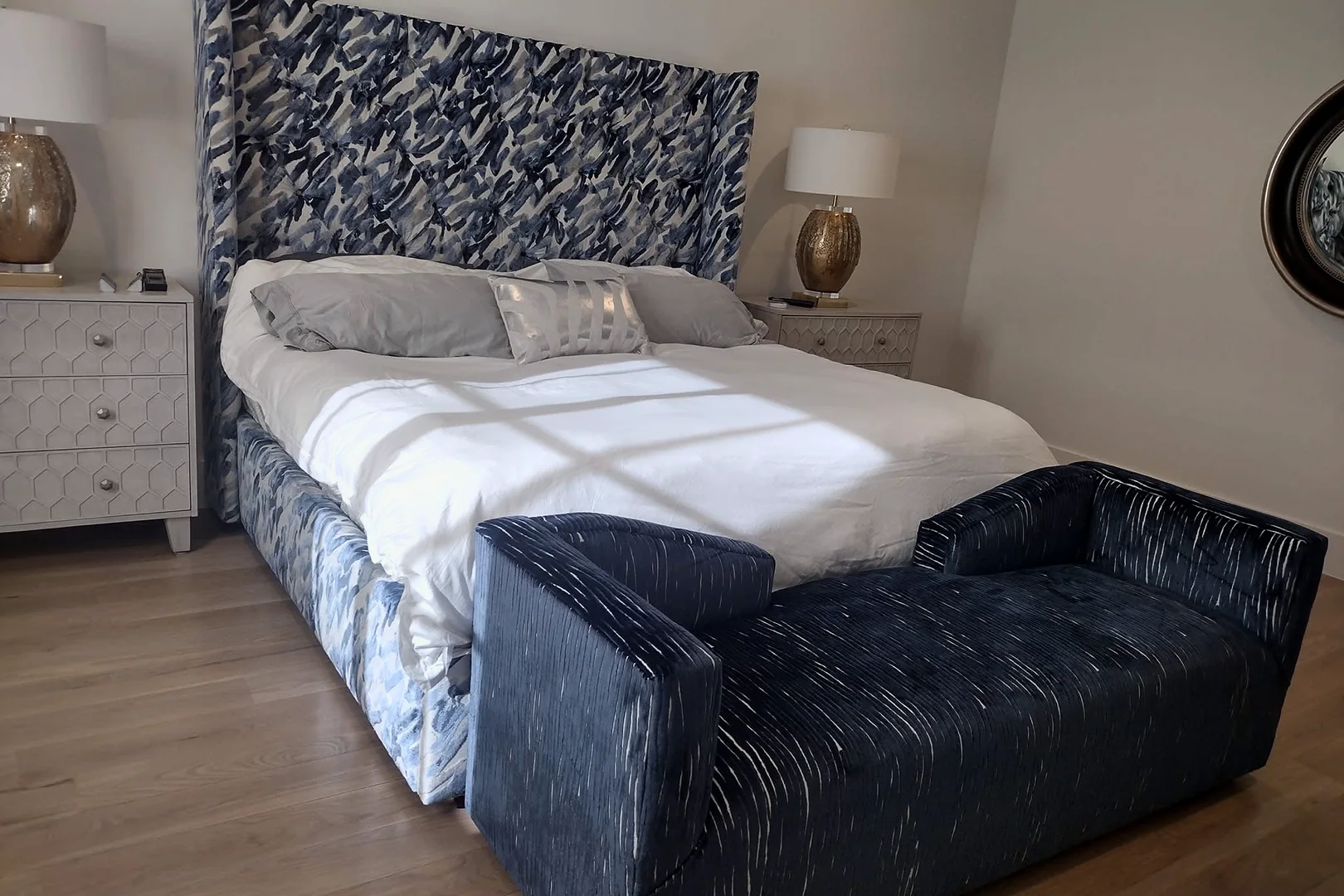 A bed with a tall blue and white patterned headboard and a navy upholstered bench with square arms at its foot