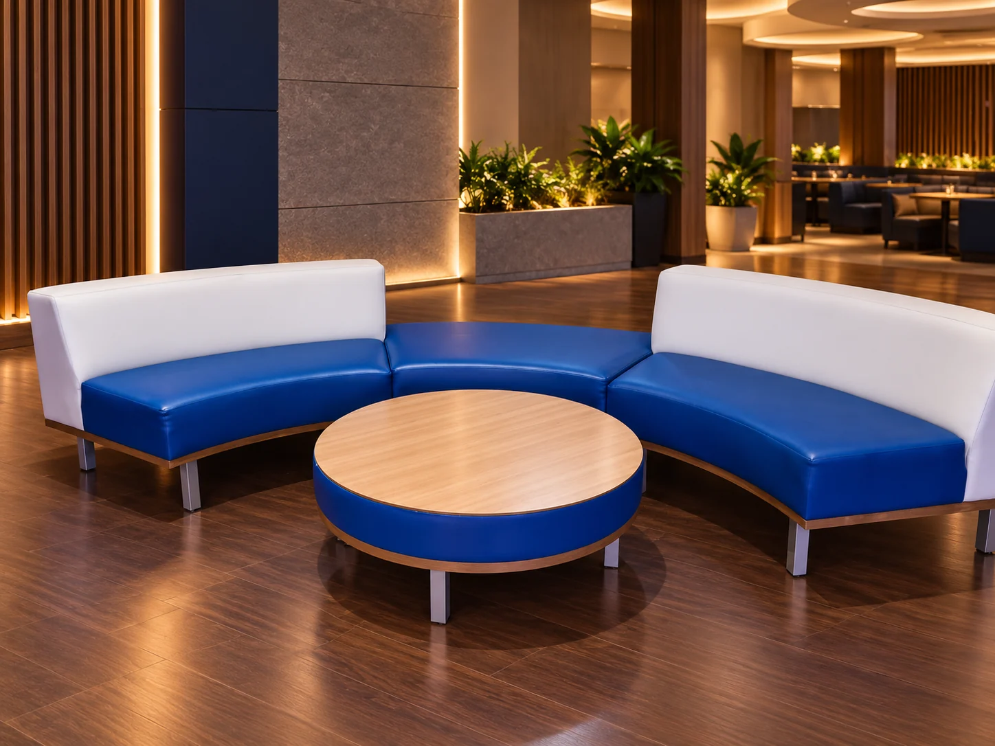 Curved banquette with blue seats and white backs around a round table with a blue edge and wood top, in a lounge with wood floors
