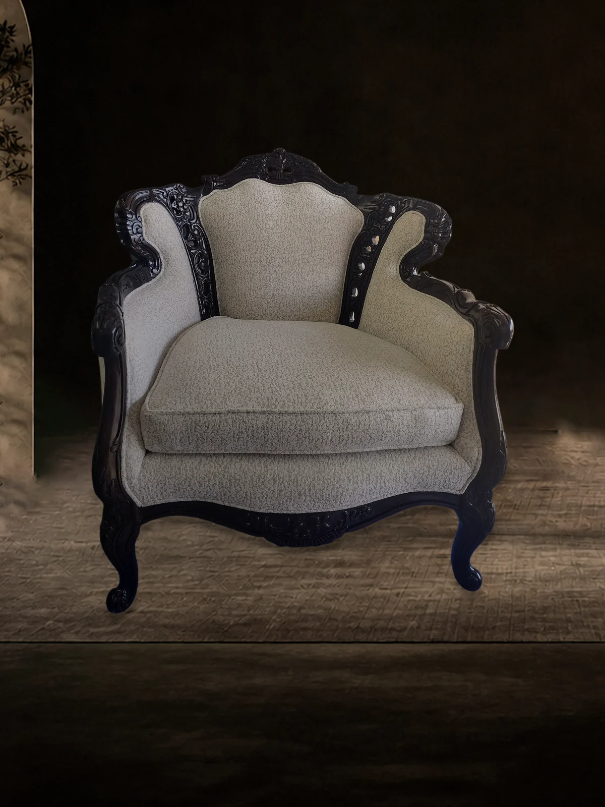 Armchair with a carved dark wood frame, cream textured upholstery and a loose seat cushion, standing on a rug