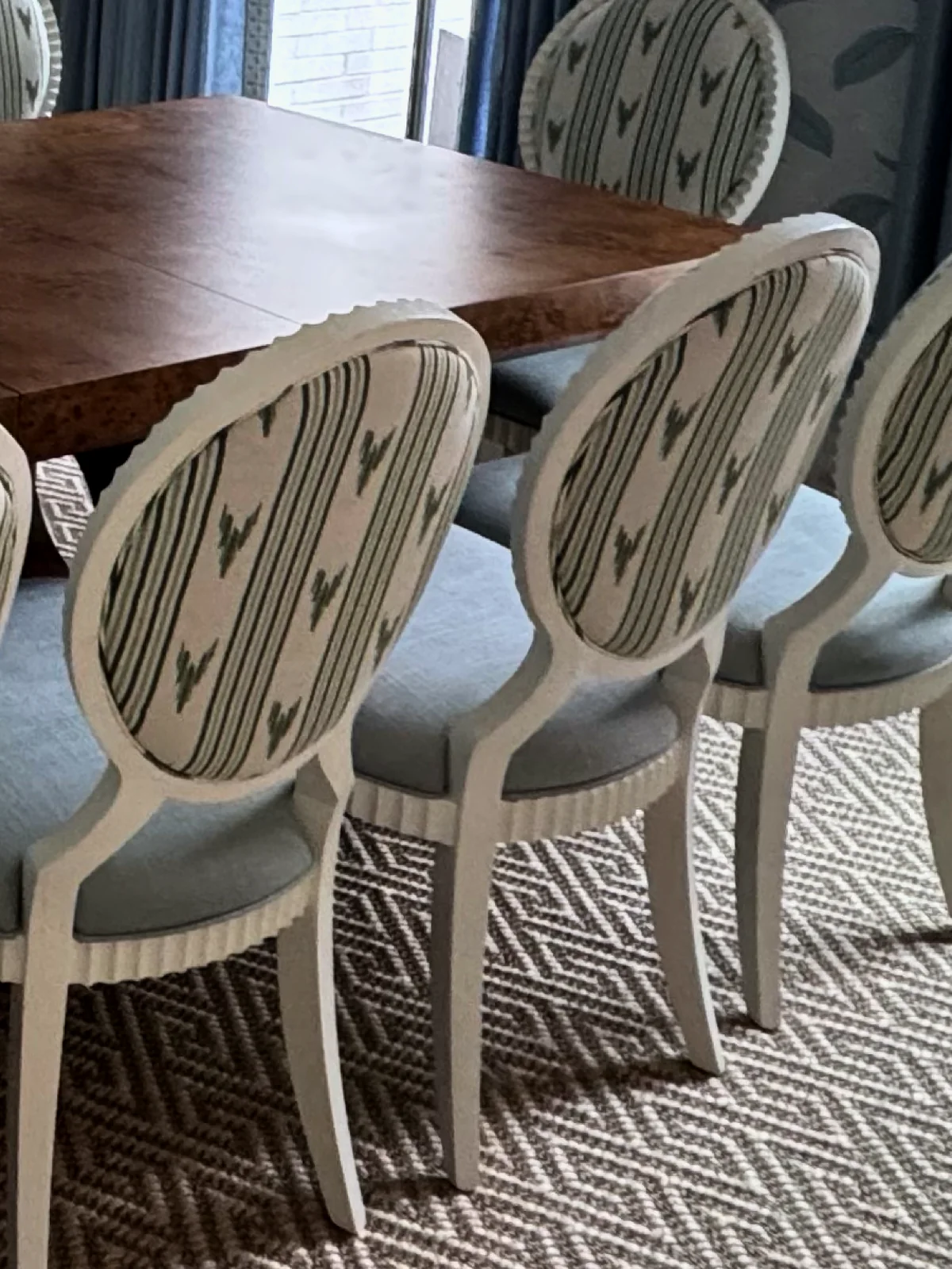 Row of oval-back dining chairs seen from behind, each back covered in the same striped fabric, with pale blue seats and white painted legs