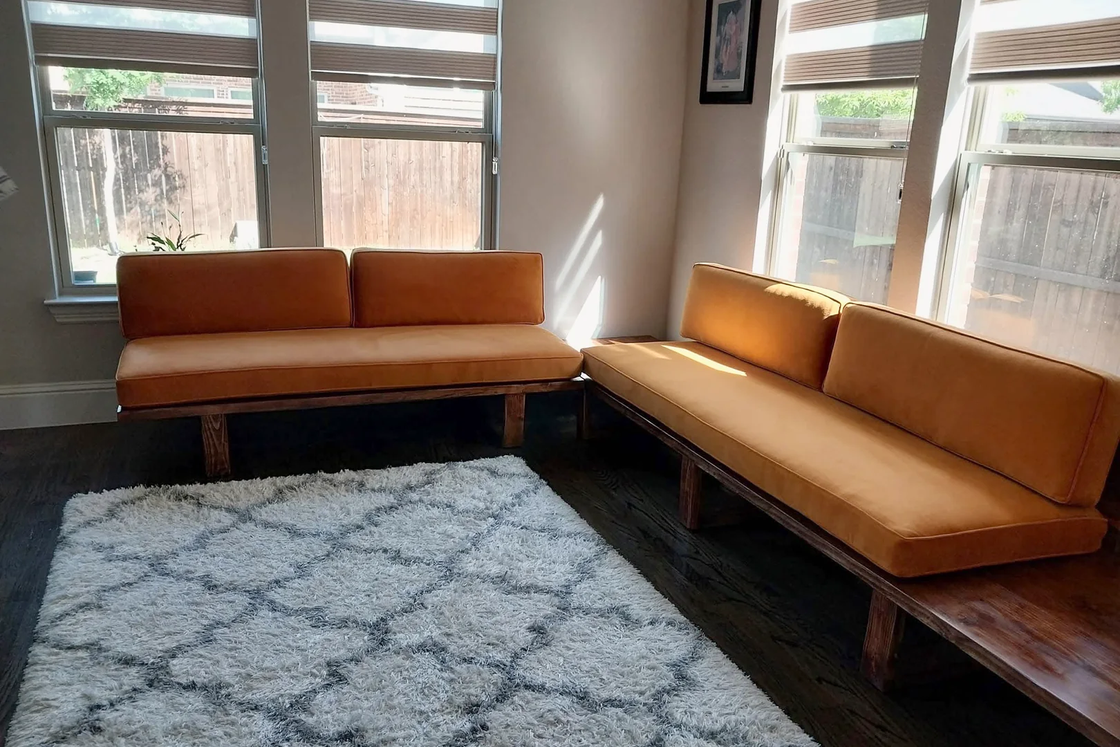 Long banquette in orange upholstery along two walls of a room, on slim wood legs, with a shaggy patterned rug in front